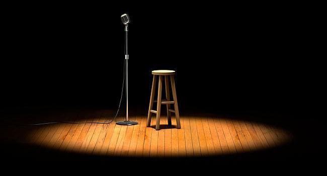 Microphone et tabouret sur une scène en bois sous la lumière d'un projecteur.
