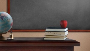 Pomme posée sur les livres du bureau du professeur, devant le tableau noir, avec une mappe monde.